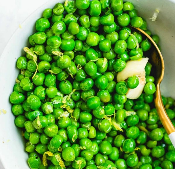 Peas with lemon in a baking dish with a spoon.