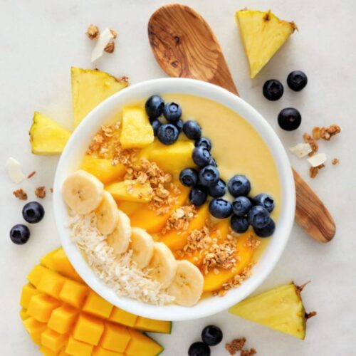 Top down view of a Pineapple Smoothie Bowl with blueberries, mango, banana, flaked coconut, and granola.