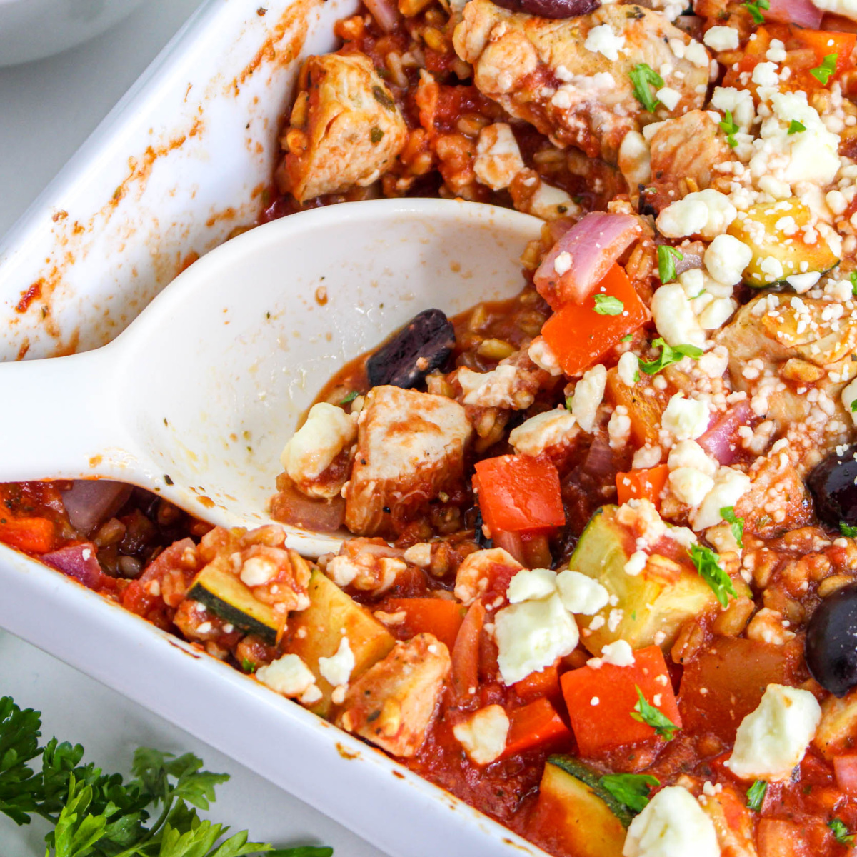 Close up of Mediterranean Chicken Bake in a casserole dish with serving spoon.