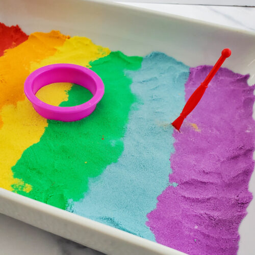Tray of homemade rainbow kinetic sand with tools.