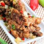 Salt and Pepper Chicken with spring onions on a white platter.