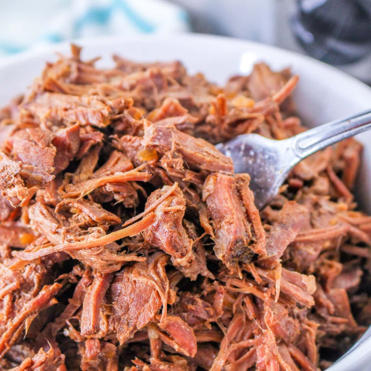 A close-up of shredded beef in a bowl, with a fork picking up some of the tender, juicy meat.