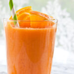Carrot Banana Smoothie garnished with fresh orange and a striped straw.