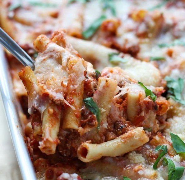 Spoon scooping Baked Ziti from a baking dish.