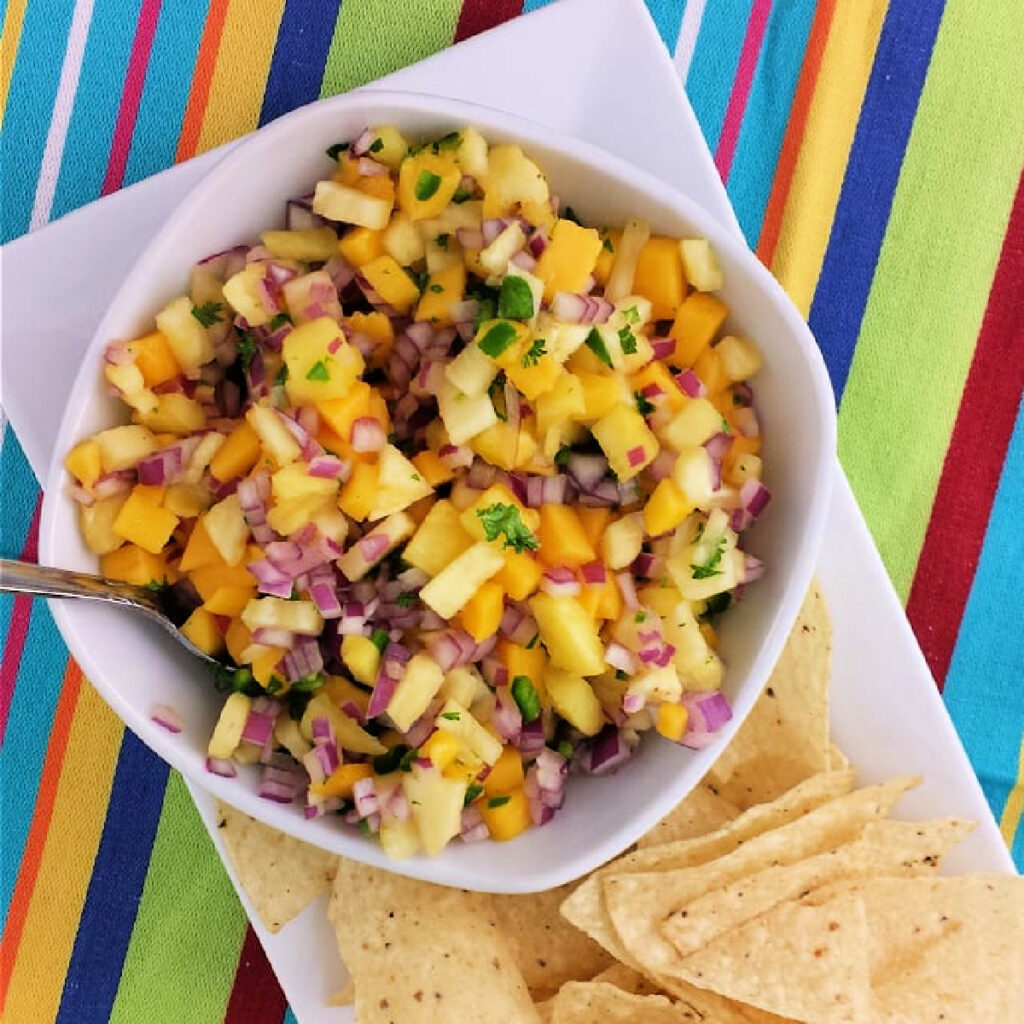 Pineapple Mango Salsa in a bowl with a spoon next to corn chips.