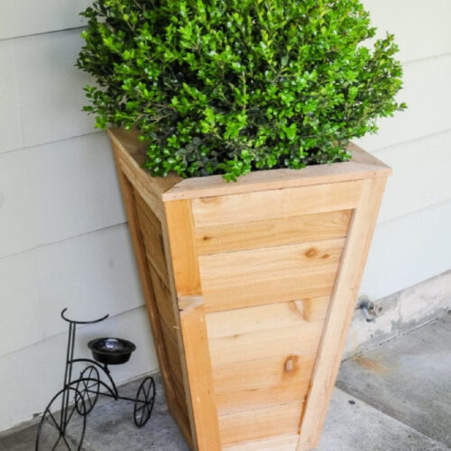A tall cedar planter box on porch with boxwood.