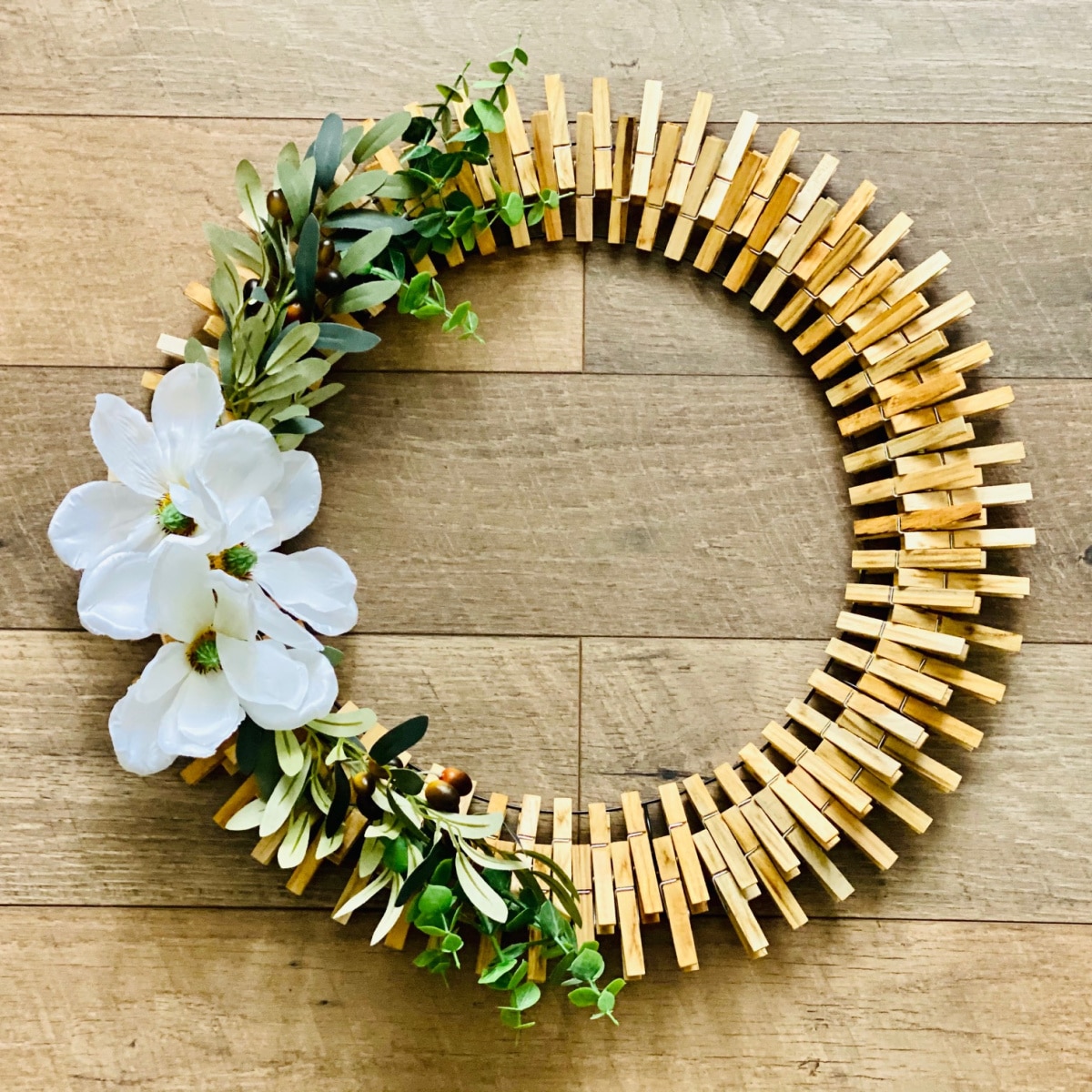 DIY Clothes Pin Wreath with greenery and magnolia flowers on a wooden background.