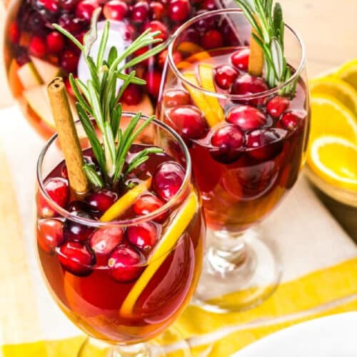 Close up image of two glasses filled with fresh cranberries and other fruits topped by cranberry sangria.