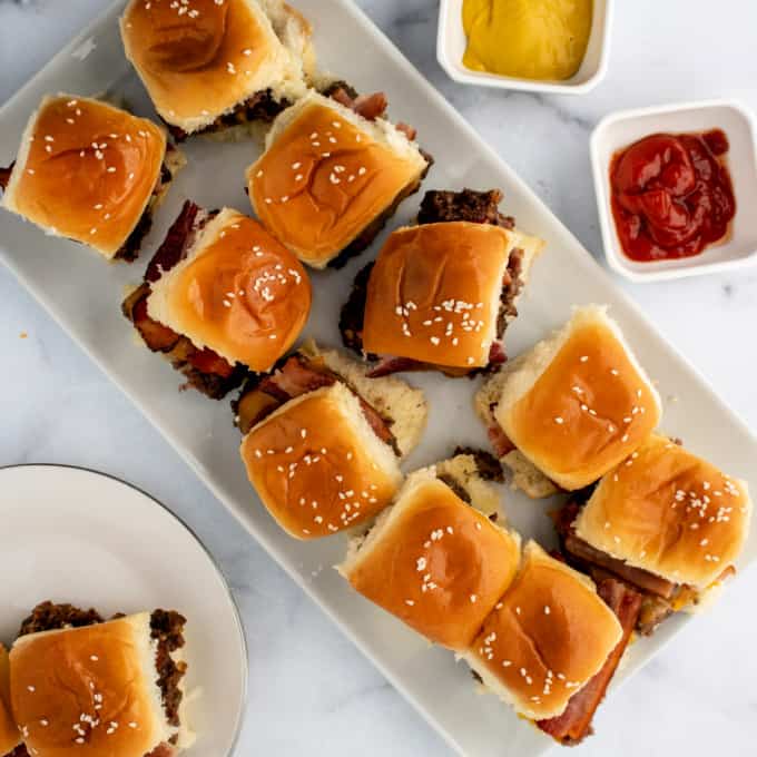 Dinner ideas using ground beef: a rectangular platter with nine slider burgers topped with sesame seed buns, sitting beside small dishes of mustard and ketchup and a plate with two more sliders.