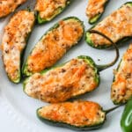 Close up of cream cheese and sausage stuffed jalapenos on a white plate.