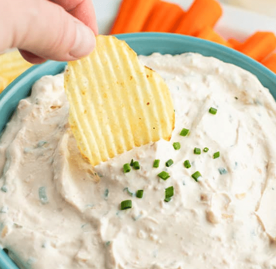 Fingers dipping a chip into french onion dip.
