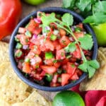 Top down view of Pico de Gallo in a bowl with a sprig of cilantro.