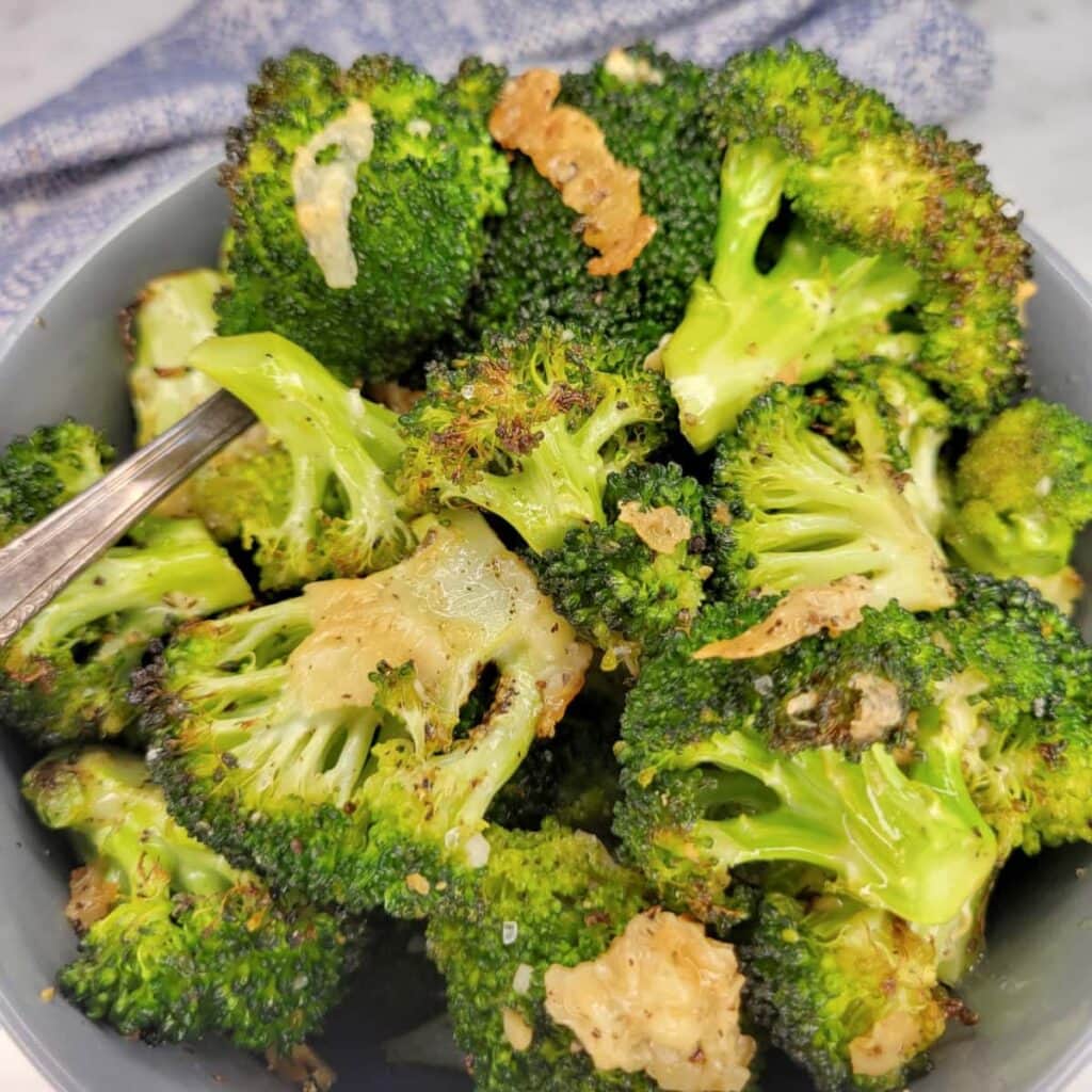 A grey bowl filled with roasted broccoli florets sprinkled with crispy garlic and salt.