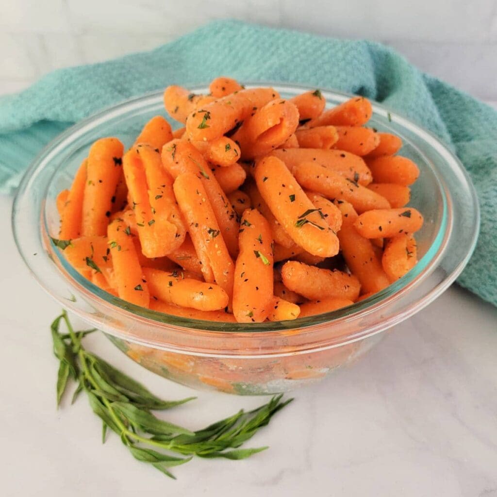 A glass bowl filled with cooked baby carrots garnished with herbs.
