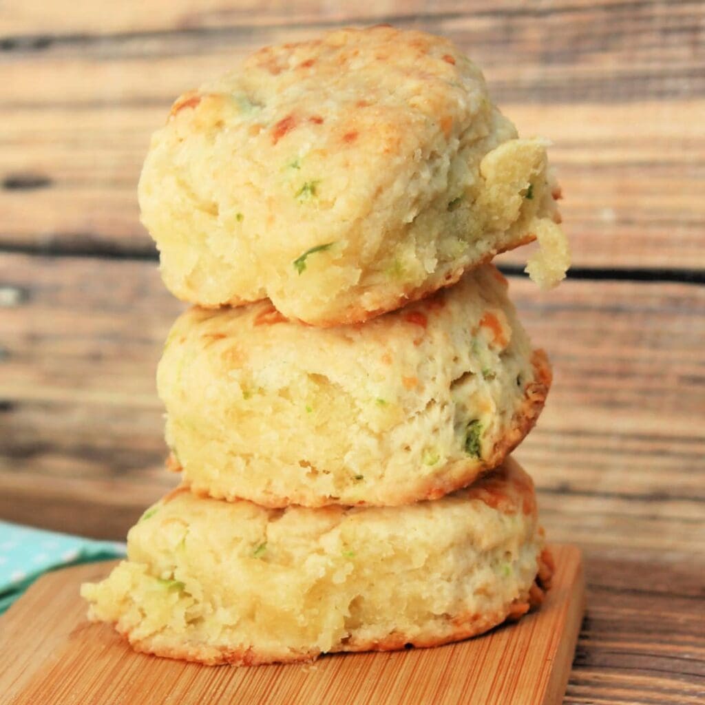 A stack of three savory cheddar and herb biscuits on a wooden cutting board.