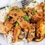 A close-up of shredded Huli Huli chicken topped with black sesame seeds and chopped green onions, served over white rice with a fork resting on the plate.