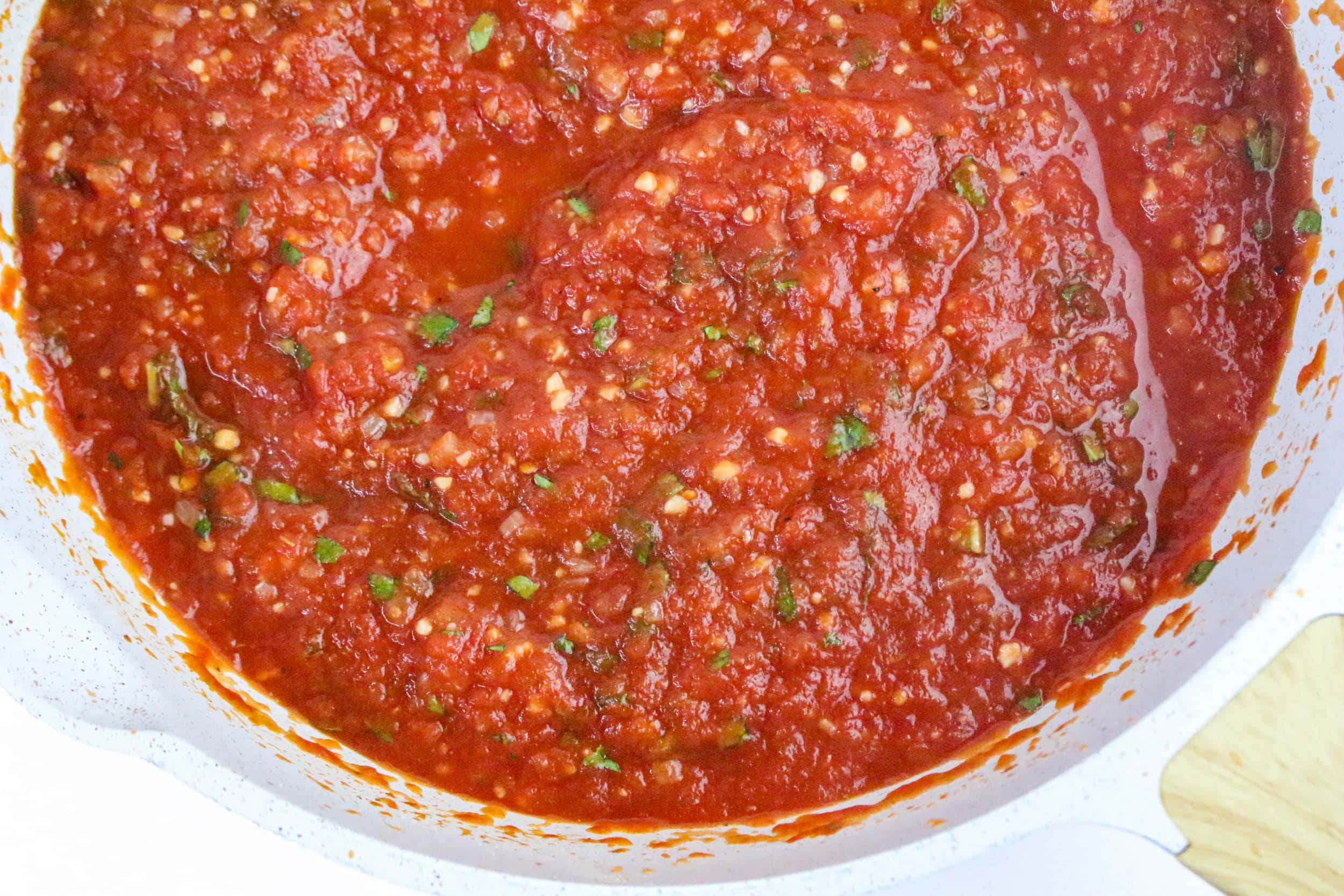 Thick, chunky red Neapolitan Pasta sauce with visible herbs and garlic, simmering in a white pot.