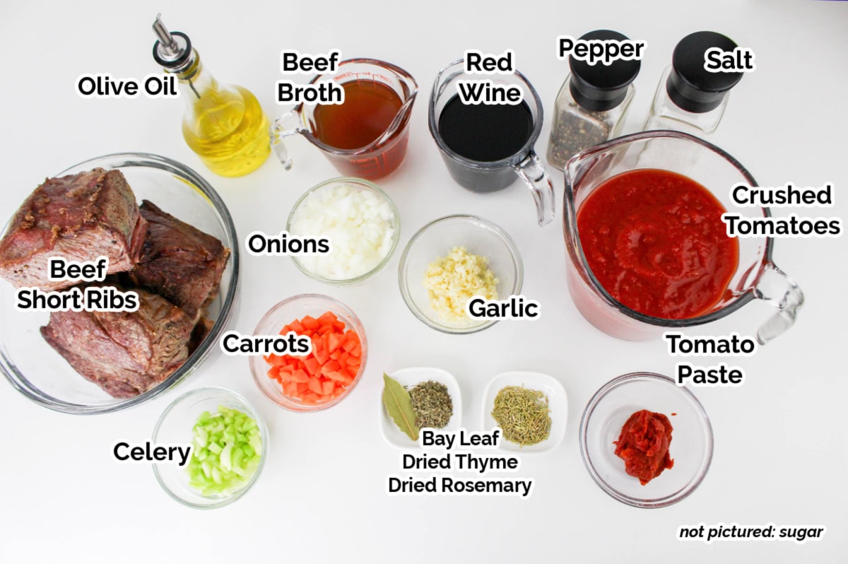 Ingredients for a Beef Short Rib Ragu, labeled: beef short ribs, onions, carrots, celery, garlic, olive oil, beef broth, red wine, bay leaf, dried thyme, dried rosemary, salt, pepper, tomato paste, and crushed tomatoes.