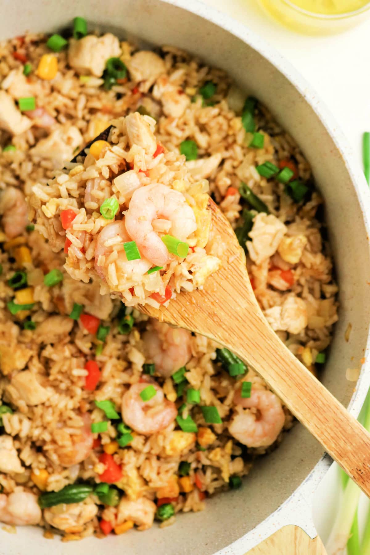 A wooden spoon lifts a portion of shrimp and chicken fried rice from a pot.
