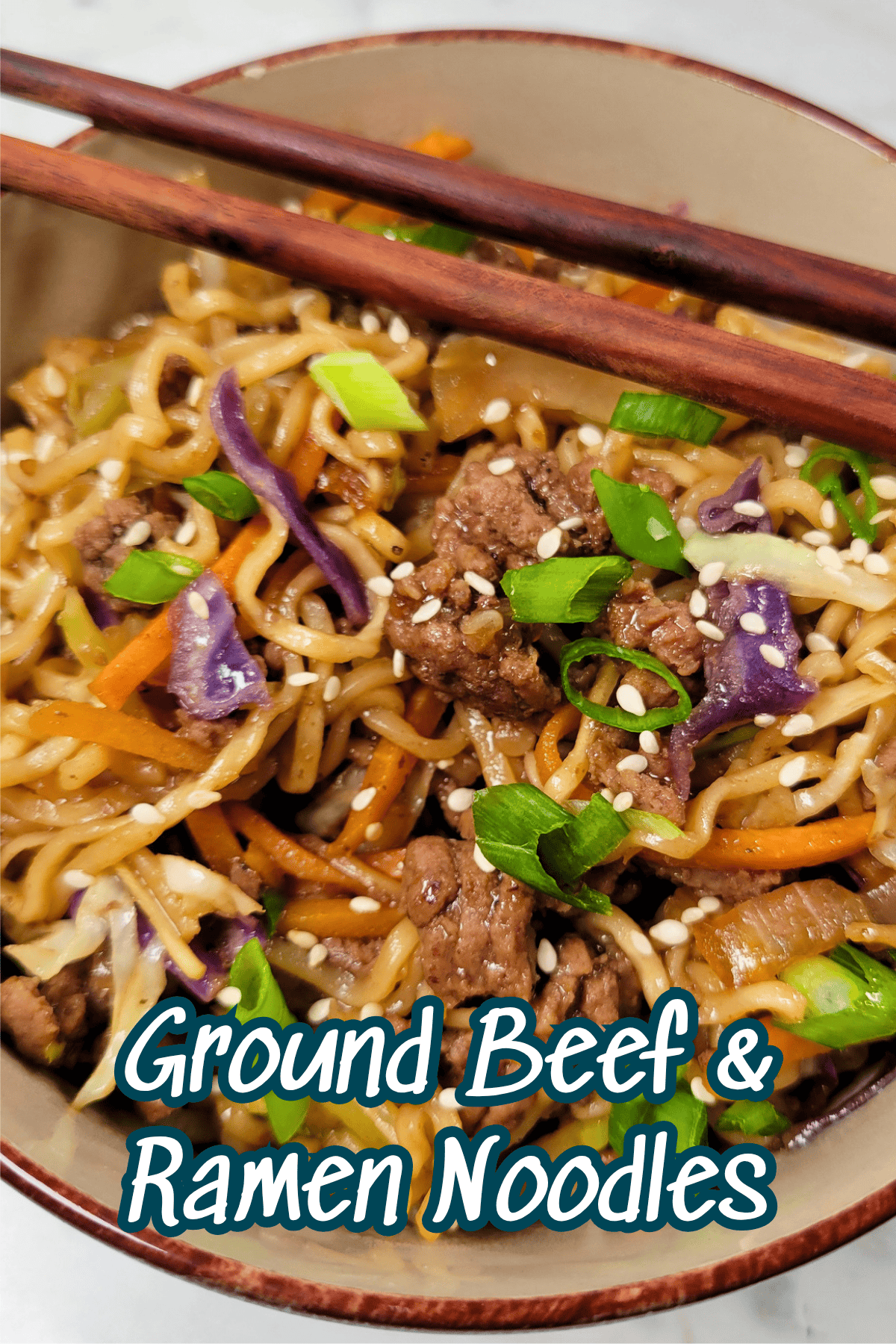 A bowl of ground beef ramen noodles mixed with shredded carrots, cabbage, green onions, and sesame seeds, topped with wooden chopsticks. The text Ground Beef & Ramen Noodles is overlaid at the bottom.