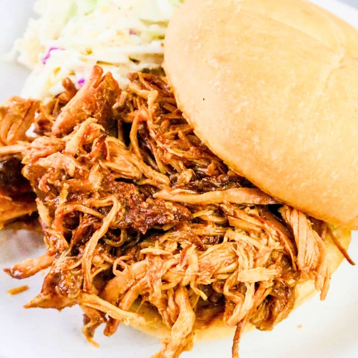 Slow Cooker BBQ Pulled Pork: a pulled pork sandwich on a bun, filled with shredded barbecue pork, is served on a plate with a side of coleslaw.