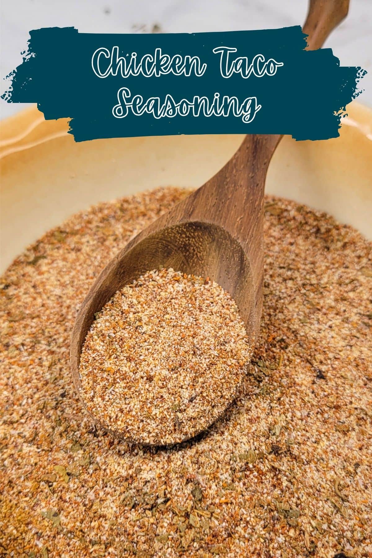 A wooden spoon scoops up homemade chicken taco seasoning from a bowl. Text at the top reads, Chicken Taco Seasoning in a handwritten style font on a teal brushstroke background.