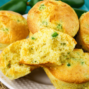 Close-up of Jiffy Jalapeno Cornbread Muffin on a white plate, with one muffin split open to reveal its moist, crumbly texture and pieces of green jalapeño inside.