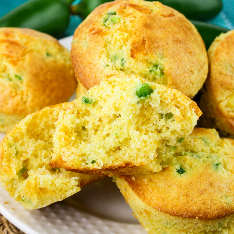 Close-up of Jiffy Jalapeno Cornbread Muffin on a white plate, with one muffin split open to reveal its moist, crumbly texture and pieces of green jalapeño inside.