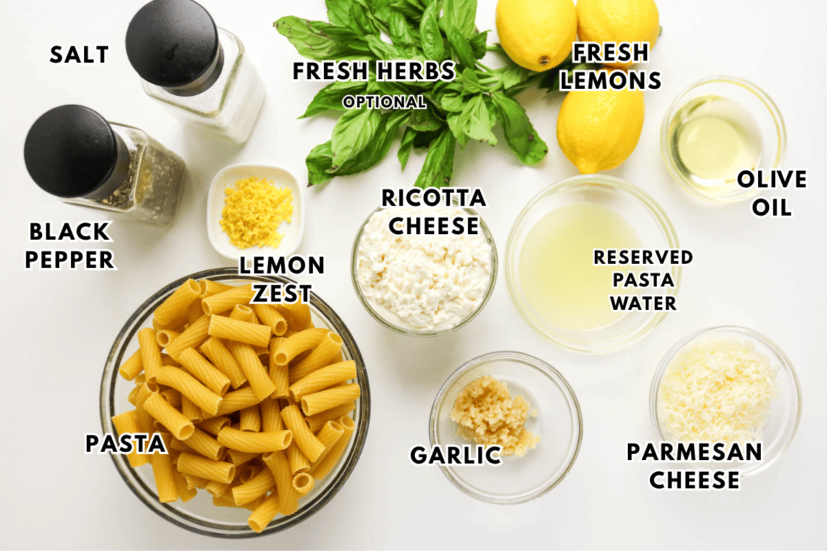 Top-down view of labeled pasta ingredients on a white surface, including rigatoni, ricotta cheese, parmesan, garlic, salt, pepper, lemon zest, fresh lemons, olive oil, reserved pasta water, and fresh herbs.