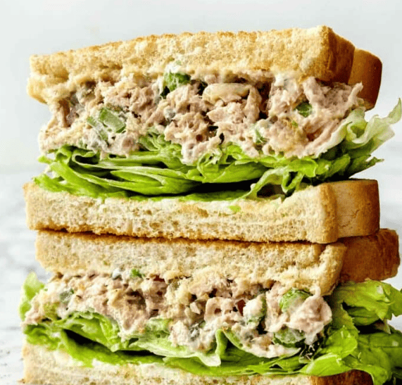 Two halves of a tuna salad sandwich stacked on top of each other, showing layers of leafy lettuce and creamy tuna salad between slices of white bread.