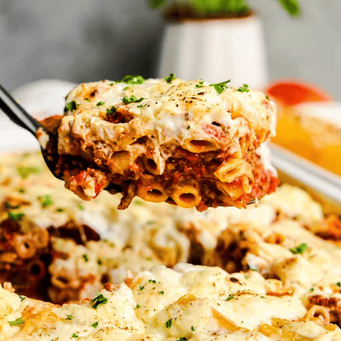 A close-up of a cheesy baked pasta slice with meat sauce being lifted from a casserole dish, topped with melted cheese and herbs—a perfect addition to your dinner ideas with ground beef. The background shows more baked pasta ready to serve.