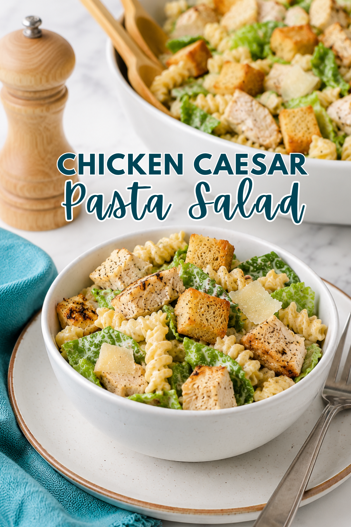A bowl of Chicken Caesar Pasta Salad with rotini pasta, grilled chicken, romaine lettuce, croutons, and Parmesan cheese, served on a plate with forks and a pepper grinder in the background.