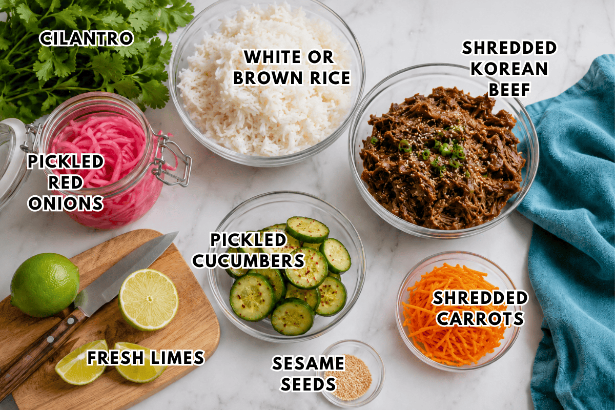 A top-down view of ingredients for a Korean Beef Rice Bowls: cilantro, white or brown rice, shredded Korean beef, shredded carrots, pickled red onions, pickled cucumbers, fresh limes, and sesame seeds on a light surface.