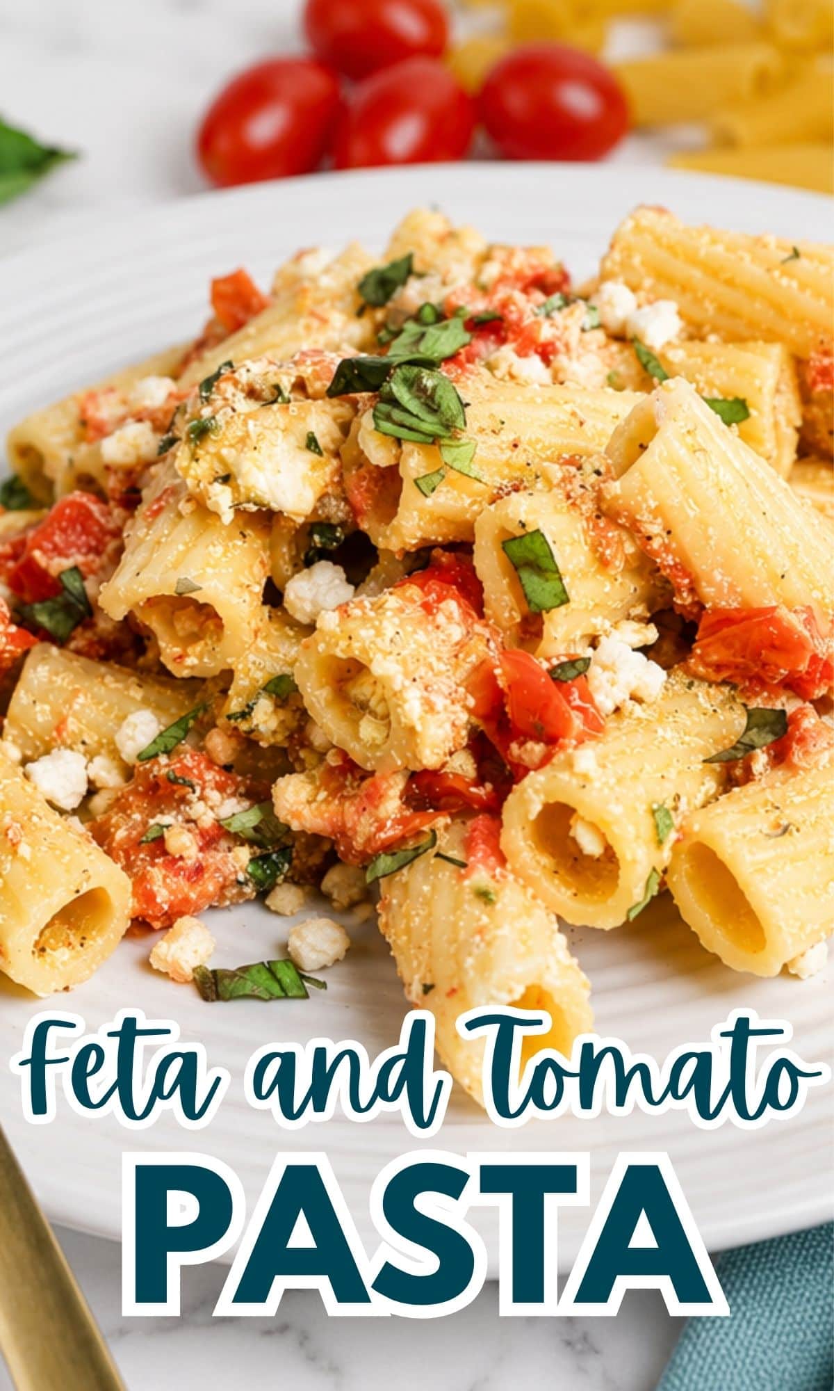A plate of rigatoni pasta with crumbled feta cheese, diced tomatoes, and fresh basil, set on a white plate. Cherry tomatoes and uncooked pasta are visible in the background. Text reads Feta and Tomato Pasta..