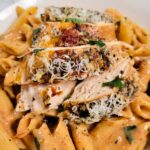 Sliced seasoned crockpot marry me chicken breast topped with grated cheese over penne pasta in a creamy tomato sauce.
