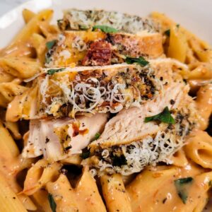 Sliced seasoned crockpot marry me chicken breast topped with grated cheese over penne pasta in a creamy tomato sauce.