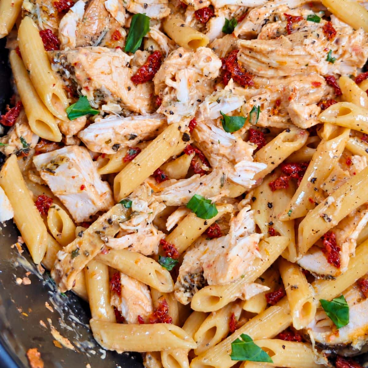 Crockpot marry me chicken featuring penne pasta tossed in a creamy sauce with shredded chicken, sun-dried tomatoes, and fresh basil.