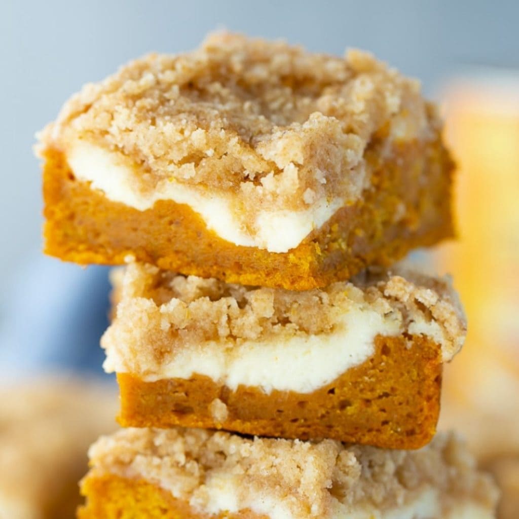 A stack of three pumpkin cream cheese bars topped with crumbs, perfect for pumpkin and cream cheese recipes.