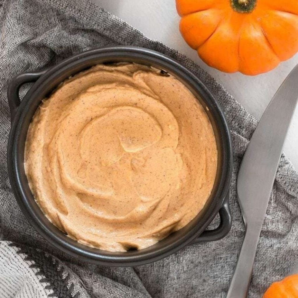 A bowl of pumpkin and cream cheese dip next to a knife and small pumpkins.