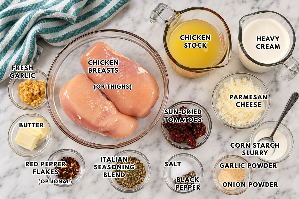 Ingredients for a crockpot marry me chicken recipe laid out on a marble surface, including chicken breasts, chicken stock, heavy cream, parmesan cheese, sun-dried tomatoes, butter, garlic, and various seasonings, all labeled with text.