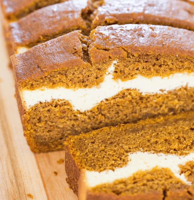 Slices of pumpkin bread layered with cream cheese filling on a wooden cutting board, perfect for pumpkin and cream cheese recipes.